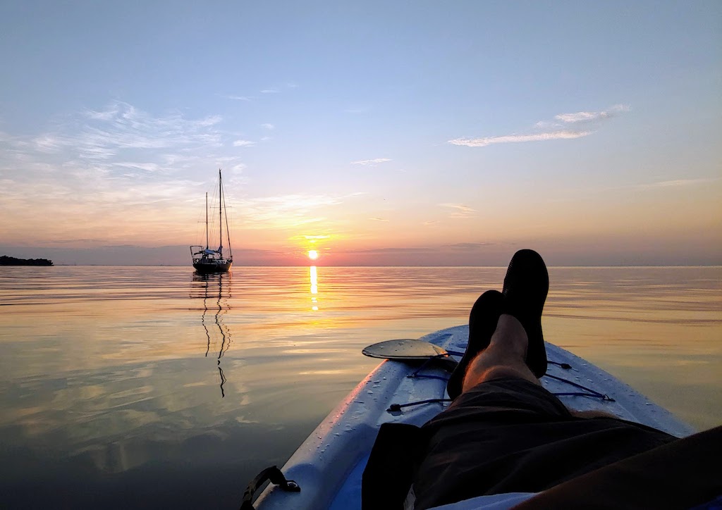 A sailboat moves to a mirror like sunrise on Lake Ontario, Canada, while it's all being observed from a stand up paddle board.